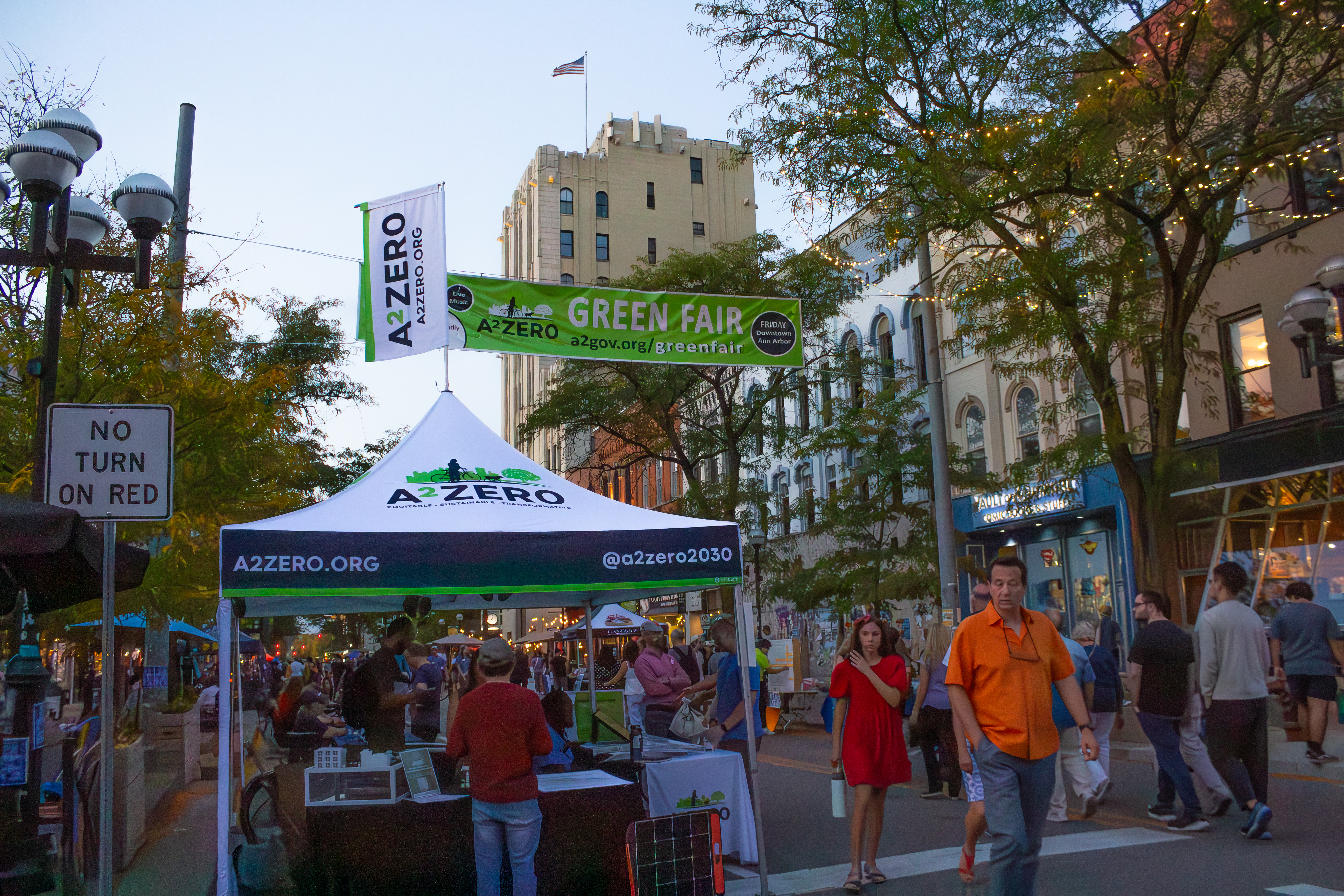 Attendees of the 2025 Green Fair walk by an A2ZERO tent and under a Green Fair banner.