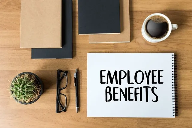 Desk with office supplies and a coffee cup on it. A pad of paper stating "Employee Benefits"