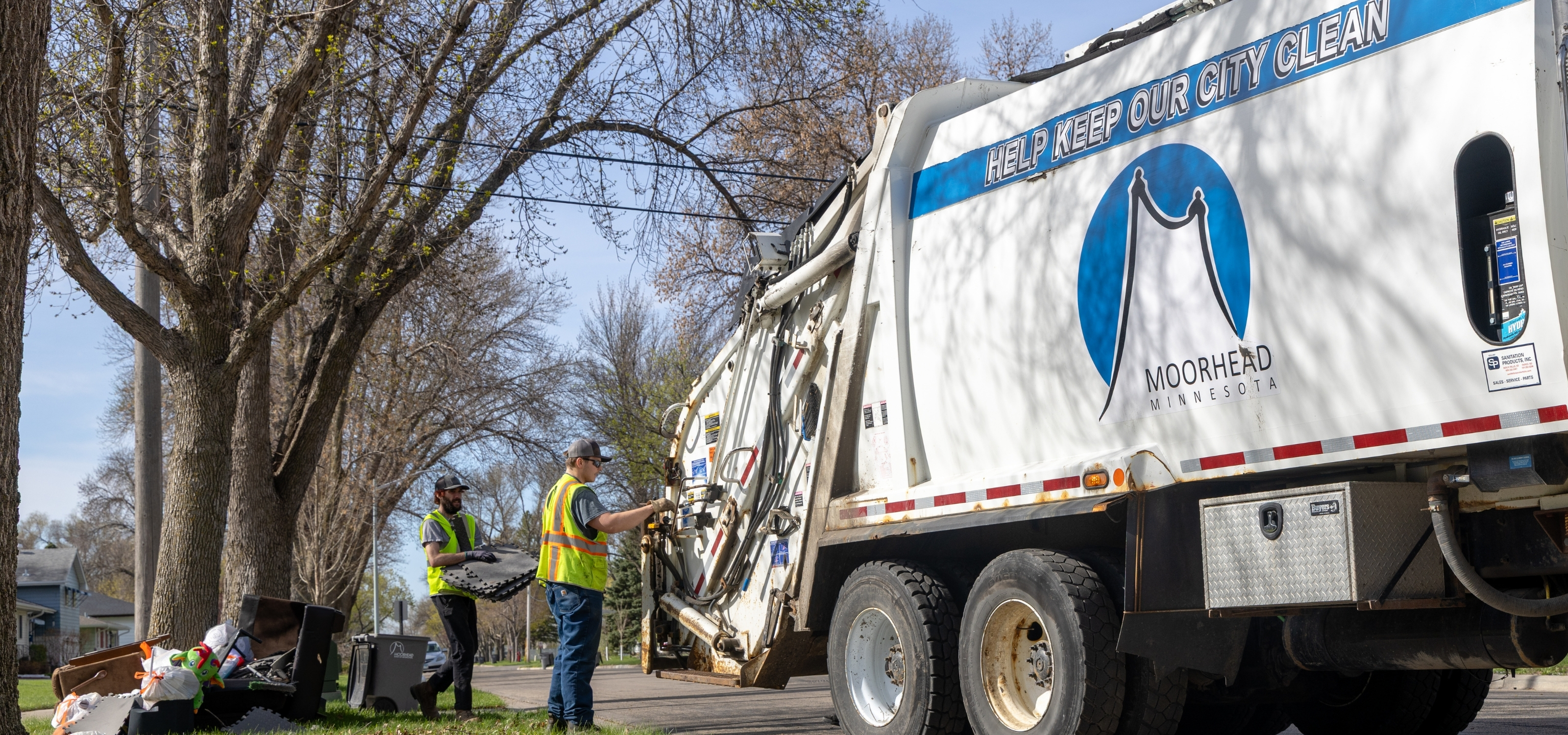 2 people load garbage from a curb into a city garbage truck