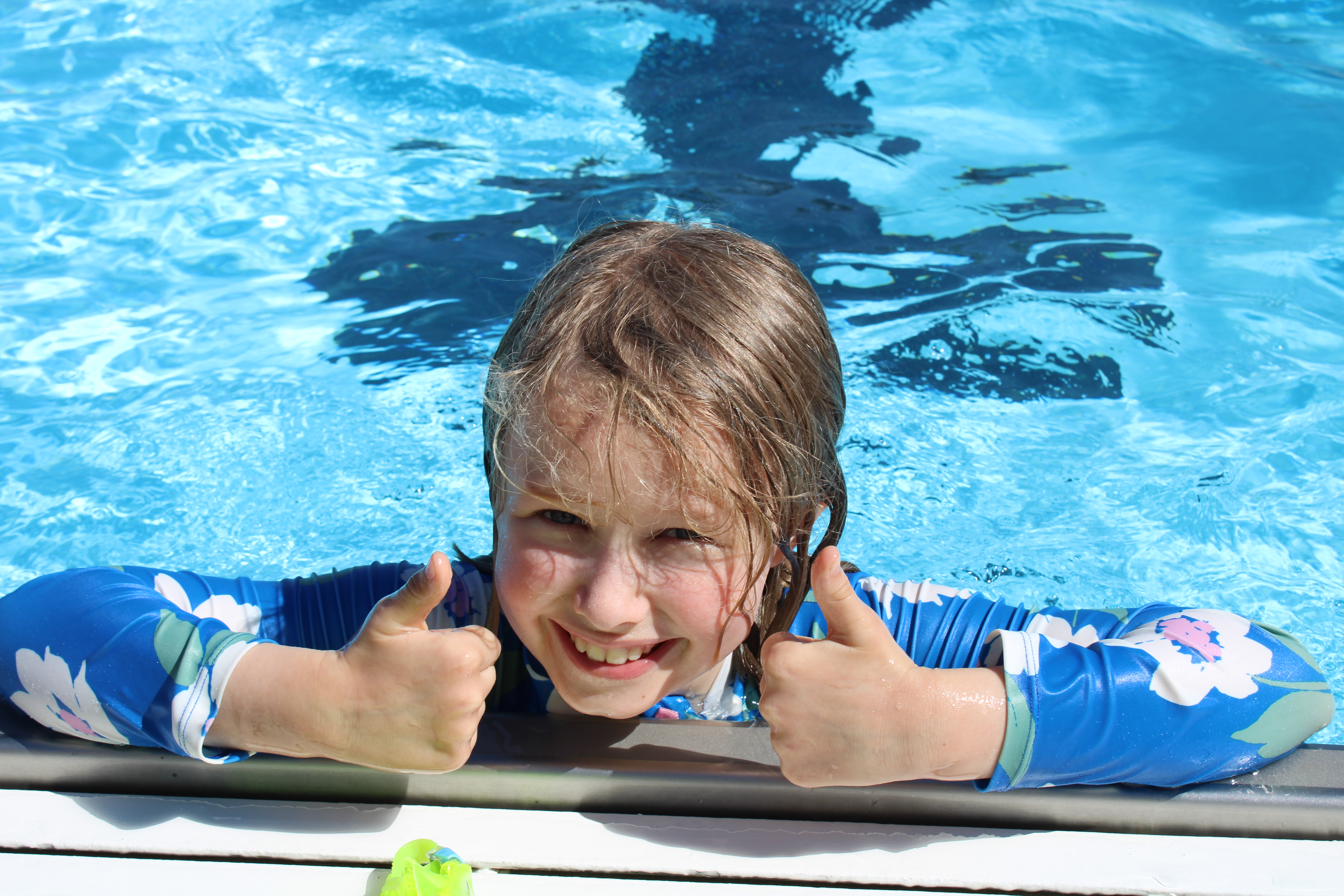 A photo of a smiling kid swimming in the pool 